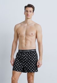 Čierne boxerky s opakujúcim sa bielym vzorom loga a elastickým pásom so značkou. Hladký povrch a voľný strih.