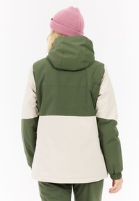 Groene en beige waterdichte jas met een capuchon, voorzien van een kleurblokontwerp en elastische manchetten. Vergezeld van een roze gebreide muts.