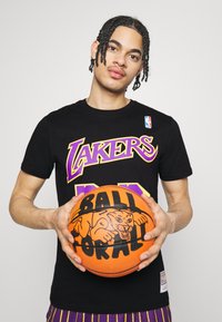 Camiseta negra con letras moradas y amarillas que dicen "Lakers". Balón de baloncesto naranja con un gráfico negro de un perro y el texto "BALL PORTAL". Pantalones cortos a rayas moradas.