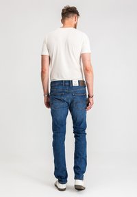 Męskie dopasowane dżinsy w głębokim niebieskim kolorze z wyblakłą fakturą, zestawione z białym bawełnianym t-shirtem. Posiadają klasyczne tylne kieszenie i skórzaną metkę.