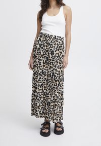 Maxi-nederdel med leopardmønster, sort elastisk talje, flydende stof og løs pasform; parret med en hvid ribbet tanktop og sorte sandaler.
