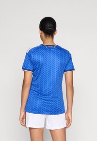 Zila sporta krekls ar lapu rakstu, īsām piedurknēm un baltu apkakli. Azzurra logo aizmugurē; saskaņots ar baltām šortiem.