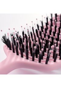 Gros plan sur une brosse à cheveux rose avec des brins noirs flexibles surmontés de petites perles roses arrondies pour un démêlage en douceur.