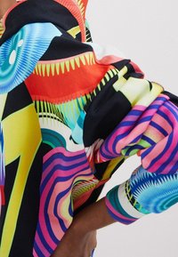 Färggad, mönstrad sweatshirt med geometriska mönster i blått, rött, gult och svart, med ribbade ärmslut och en avslappnad passform.