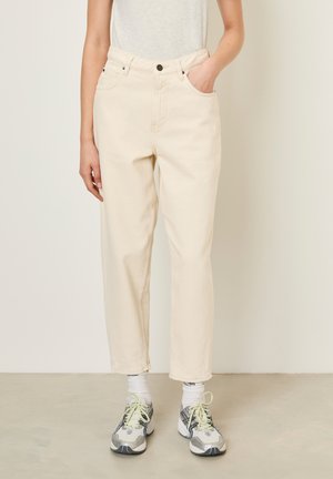 Cream-colored denim pants with a straight fit, five pockets, and a button closure. Paired with gray and yellow athletic shoes.