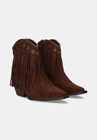 Botas de tobillo de ante marrón con detalles de flecos, acentos de botón de latón, punta afilada y tacón bajo apilado. Cierre lateral con cremallera para facilitar el uso.