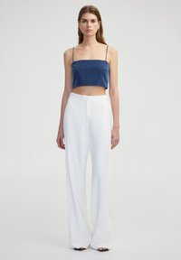 Námořnický crop top se špagetovými ramínky, kombinovaný s bílými kalhotami s vysokým pasem a širokými nohavicemi. Hladké textury, minimalistický design a žádné viditelné vzory.