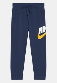 Navyblå joggers i mjukt tyg har ett elastiskt midjeband med dragsko. Framtstående gul och vit "NIKE"-logotyp på sidan.