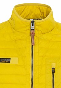 Gul quilted jakke med høj krave, frontlynlås og venstre brystlomme. Har læder lynlåsstræk og mærketikette.