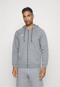 Grå zip-up hettegenser laget av mykt materiale, med en front glidelås, ribbet mansjetter og hette. Under Armour-logoen er vist på brystet.