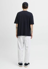 Crna oversized majica, sivi dukserice s stražnjim džepom, crna kapa i tenisice; minimalistički dizajn, mješavina pamučnih tkanina.