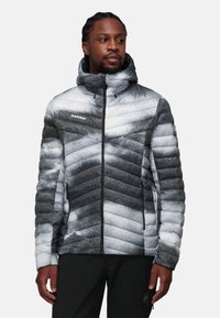 Giacca imbottita nelle tonalità di grigio e bianco con un motivo a zig-zag, chiusura con zip e cappuccio. Realizzata in materiale leggero e isolante.