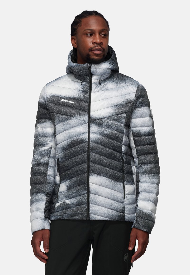 Giacca imbottita nelle tonalità di grigio e bianco con un motivo a zig-zag, chiusura con zip e cappuccio. Realizzata in materiale leggero e isolante.