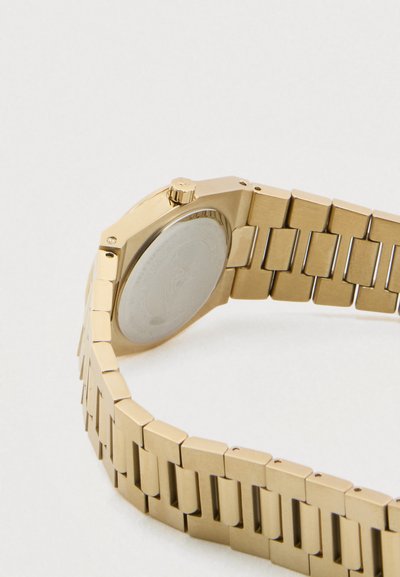 Χρυσό μεταλλικό ρολόι χειρός εμφανιζόμενο από πίσω με βραχιόλι συνδεδεμένων κρίκων και κορώνα σε λευκό φόντο.