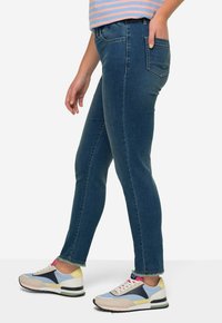 Jeans de mezclilla azul oscuro con un corte ajustado, que presentan un acabado desteñido, diseño de cinco bolsillos y un dobladillo ligeramente desgastado, combinados con zapatillas multicolores.