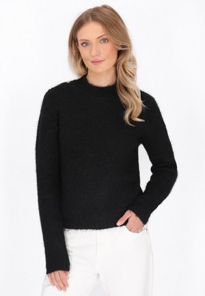 Maglione nero morbido con collo rotondo e maniche lunghe. Presenta bottoni decorativi sulla spalla. Tessuto soffice. Abbinato a pantaloni bianchi.