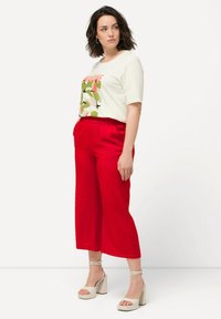 Witte t-shirt met korte mouwen en kleurrijke grafische print; rode, ruime broek; beige hoge hakken met enkelbandjes.
