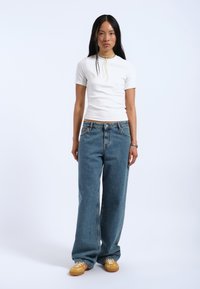 Hvid kortærmet skjorte, blå vide denim jeans og gule sko med farverige snørebånd. Enkelt design med et afslappet look.