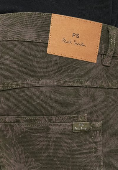 Hlače od tamnog uzorkovanog materijala s dva vidljiva Paul Smith oznake, jednom kožnom oznakom na pojasu i jednom malom fabric oznakom na rubu džepa.