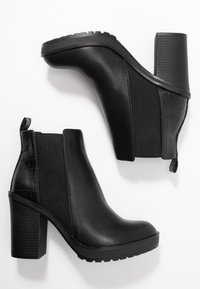 Bottines noires avec un dessus en cuir brillant, des panneaux latéraux texturés et un talon épais avec un accent à motifs et une languette à l'arrière.