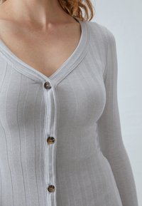 Gray ribbed cardigan with long sleeves, V-neckline, and button closure. Features textured fabric and brown buttons for detail.