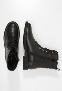 Černé kožené kotníkové boty s šněrováním vpředu, bočním zipem a robustní gumovou podrážkou. Obsahují stříbrné okénka a hladký povrch.