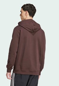 Sweat à capuche marron avec une texture douce, doté d'une grande capuche arrière et de poignets côtelés, associé à un pantalon de sport noir.