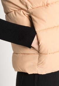 Brzoskwiniowa kurtka puchowa z czarnym ściągaczem na rękawach. Posiada boczną kieszeń i pikowaną fakturę, podkreślającą ciepło i komfort.