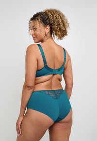 Il reggiseno teal e le mutandine a vita alta presentano un tessuto morbido con dettagli in pizzo sul retro. Spalline regolabili e chiusura a gancio per una vestibilità perfetta.