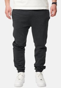 Schwarze Jogginghosen aus weichem Stoff mit tailliertem Design, ausgestattet mit elastischen Bündchen und Seitentaschen. Kombiniert mit weißen Sneakers.