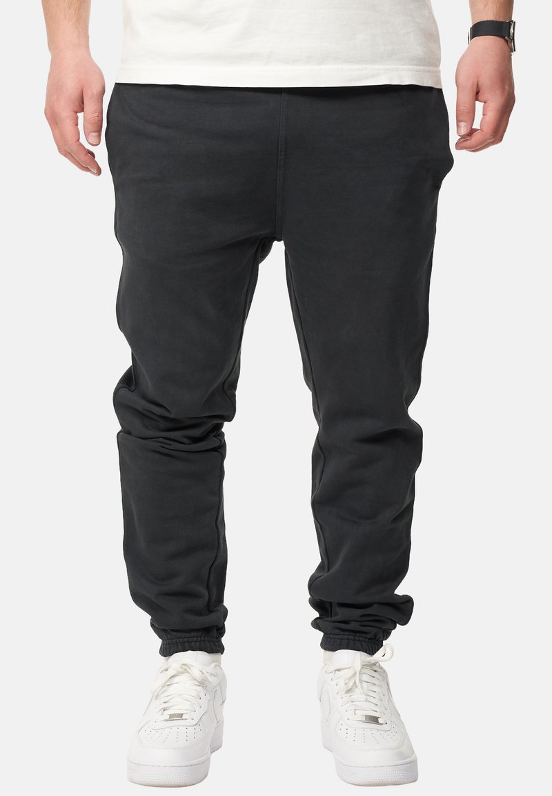 Schwarze Jogginghosen aus weichem Stoff mit tailliertem Design, ausgestattet mit elastischen Bündchen und Seitentaschen. Kombiniert mit weißen Sneakers.