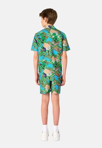 Conjunto de camisa de manga corta y pantalones cortos, con un fondo azul que presenta un diseño pixelado de casas, personajes y vegetación.
