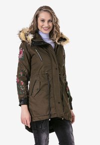 Olivgrüne Parkajacke mit einer Kapuze aus Kunstfell, floralen Stickereien und Verzierungen an den Ärmeln, mit Reißverschluss- und Druckknöpftaschen sowie verstellbarem Kordelzug.