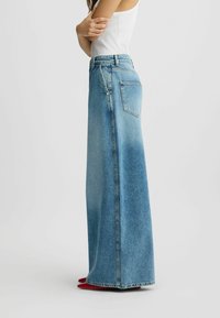 Gonna maxi in denim celeste chiaro con vestibilità ampia, vita alta e orli grezzi. Presenta una tasca sul retro e dettagli delle cuciture sui lati.