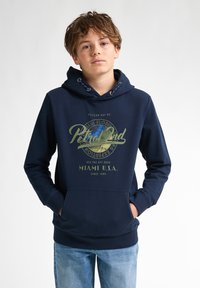 Sudadera navy con bolsillo frontal, capucha con cordón, y estampado de logotipo que presenta "Pelican Bay Dr" y "Miami U.S.A." en colores contrastantes.