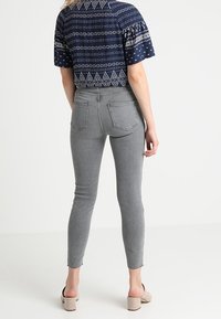 Jeans skinny de talle alto en gris con un diseño ajustado, que cuentan con bolsillos traseros y dobladillos sin deshacer. Combinados con una blusa de patrón azul marino.