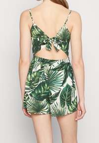 Conjunto de dos piezas con estampado tropical verde que incluye una blusa con lazo en la espalda y pantalones cortos, fabricado con tejido ligero, de textura suave y con cintura elástica.