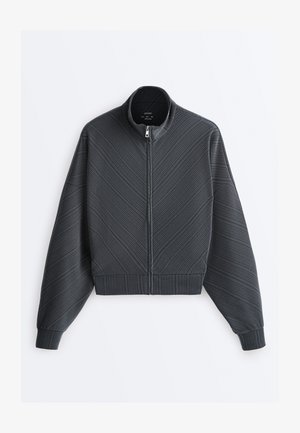 Dunkelgraue Zip-up-Jacke mit diagonaler Rippstruktur, hohem Kragen, langen Ärmeln sowie gerippten Bündchen und Saum.