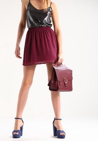 Top sin mangas metálico plateado, falda plisada granate, sandalias de plataforma azules y bolso burdeos con detalle de anillo metálico.