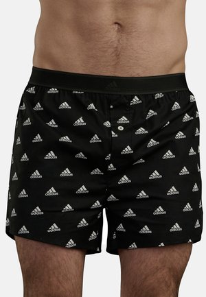 Svarta boxerkalsonger med små vita Adidas-logotyper i ett upprepat mönster, med svart elastisk midjeband och knappgylf.