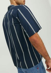 Tamsiai mėlyna trumpomis rankovėmis marškiniai su baltais vertikaliais raštais, turintys klasikinį apykaklę ir laisvą siluetą, pagaminti iš lengvos medžiagos.