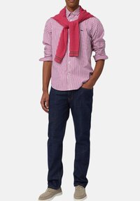 Gestreepte rood-witte overhemd met een kraag, met een getextureerde roze trui om de schouders geknoopt, gecombineerd met donkerblauwe jeans en beige schoenen.