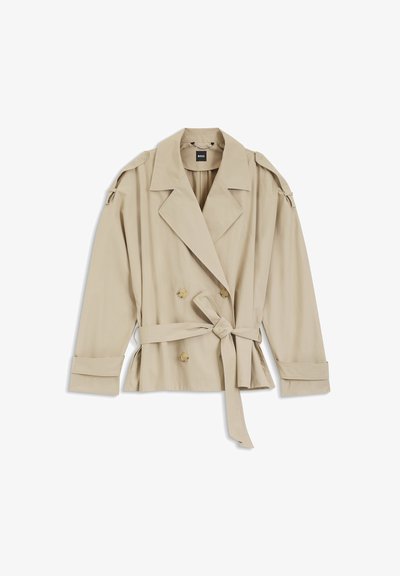 Trench-coat beige à double boutonnage avec larges revers, taille ceinturée, poignets boutonnés et épaulettes, posé à plat sur fond blanc.