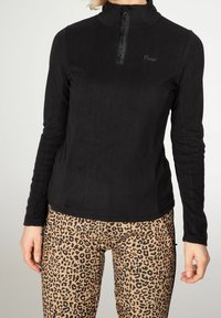 Sudadera de forro polar negro con cuello alto y media cremallera en la parte frontal, con una textura suave. Combinada con pantalones de estampado de leopardo beige.