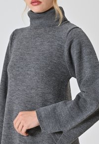 Maglione grigio a collo alto lavorato a maglia con maniche lunghe e fessure laterali. Morbida texture e vestibilità comoda, con colletto e polsini a coste.