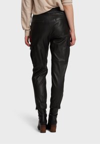 Svarta läderbyxor med avslappnad passform, elastisk midja och samlade manschetter. Inkluderar sidfickor och en mjuk textur.