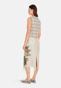 Beiger karierter Cropped-Top ohne Ärmel, kombiniert mit einem hellgrauen Midikleid mit floralem Muster und Rückenschlitz. Silberschuhe.