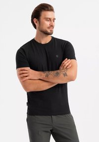 Czarny bawełniany T-shirt z okrągłym dekoltem, krótkimi rękawami i małym logo na piersi; w połączeniu z szarymi spodniami.