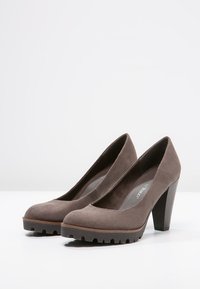 Zapatos de tacón alto de ante marrón con puntera redondeada, suela de goma y detalles texturizados, que cuentan con un tacón de bloque de 5 cm.