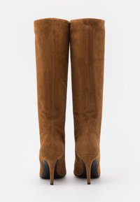 Bruine suède laarzen tot over de knie met een slank silhouet, naaldhakken en een gladde textuur, voorzien van een afgeronde bovenkant en zonder zichtbare hardware.